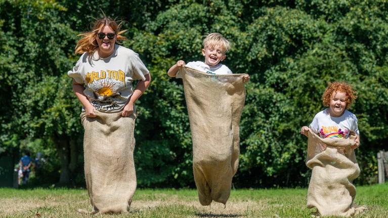 A family jumping in a sack race in the gardens of Felbrigg Hall, Norfolk